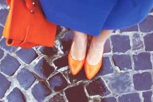 Women's legs in orange shoes. Bright orange shoes and bag. Blue coat, orange classic ladies shoes and tote bag. Rainy day. Street fashion. Street style. Business casual look. Autumn outfit.
