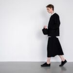 Person i svart ton-i-ton-outfit med plisserad kjol och sneakers