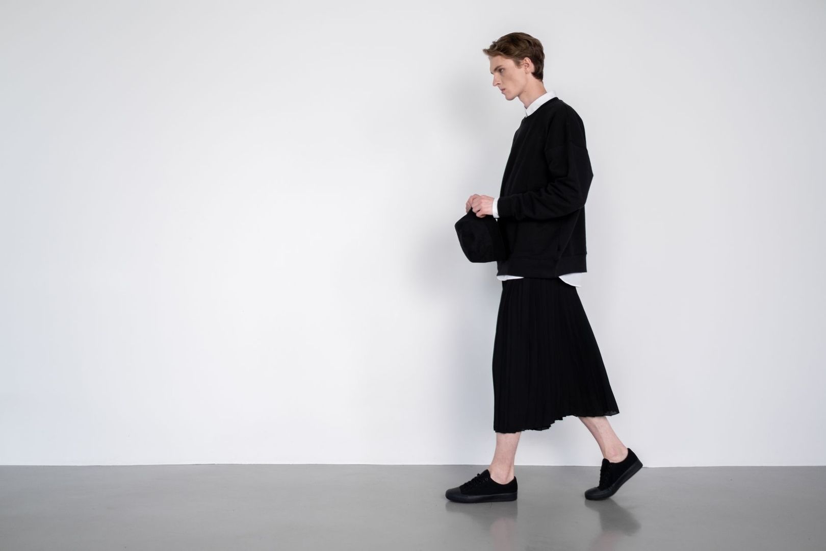 Person i svart ton-i-ton-outfit med plisserad kjol och sneakers